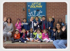 Adults and children waving in front of a building with a "Little Dolphin" sign