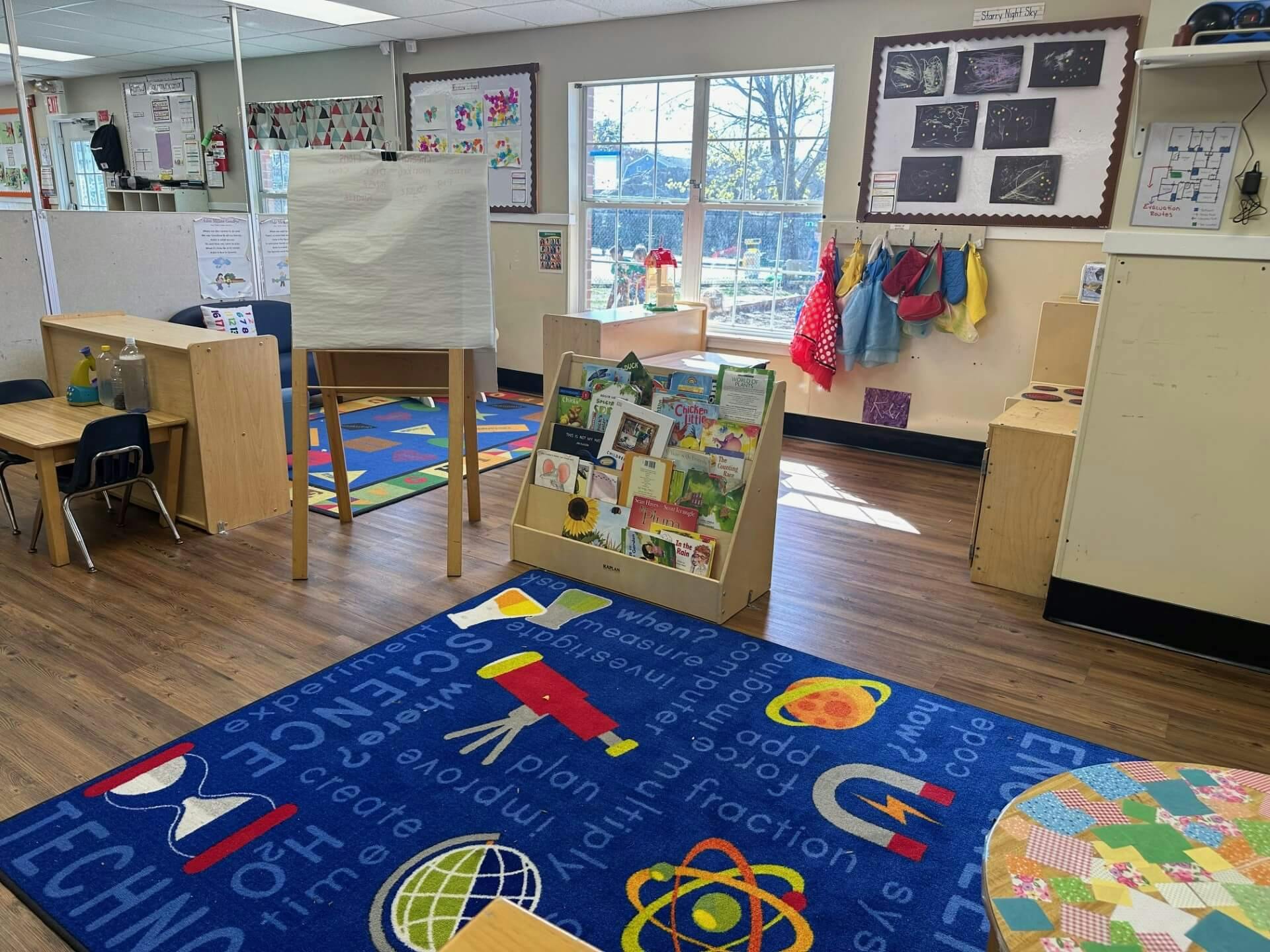 Classroom with a blue rug, small tables, and a bookshelf with children's books