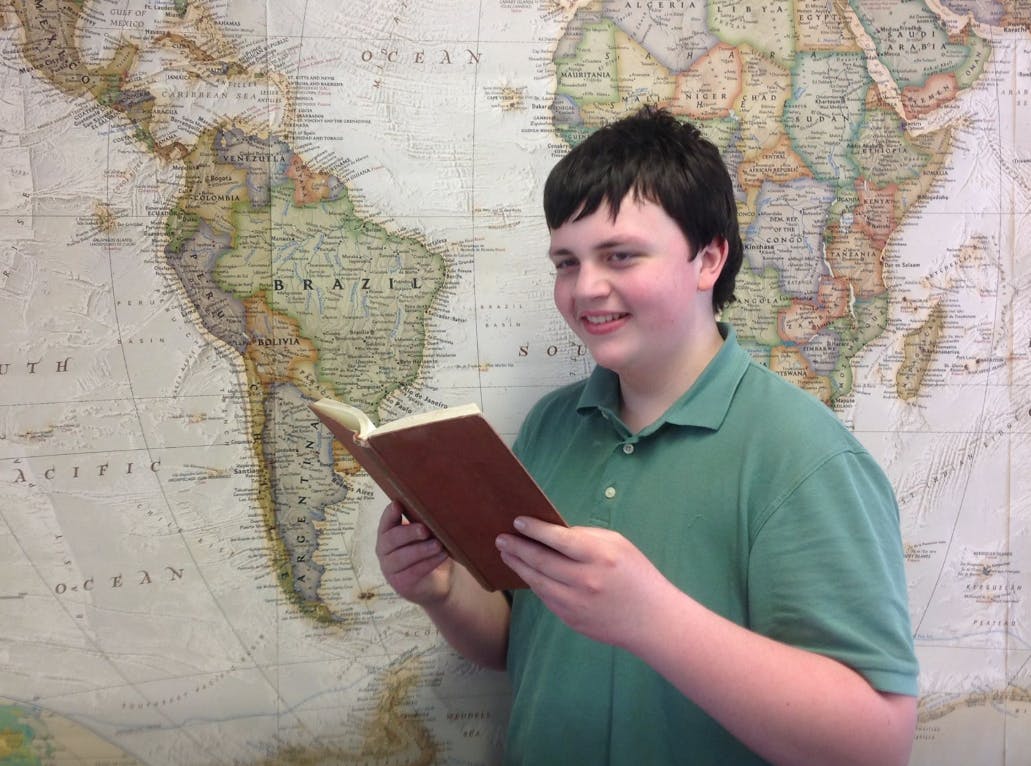 Teen reading a book in front of a world map