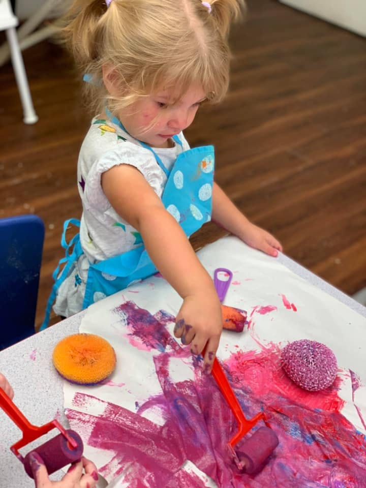 Child in an apron painting with rollers and sponges