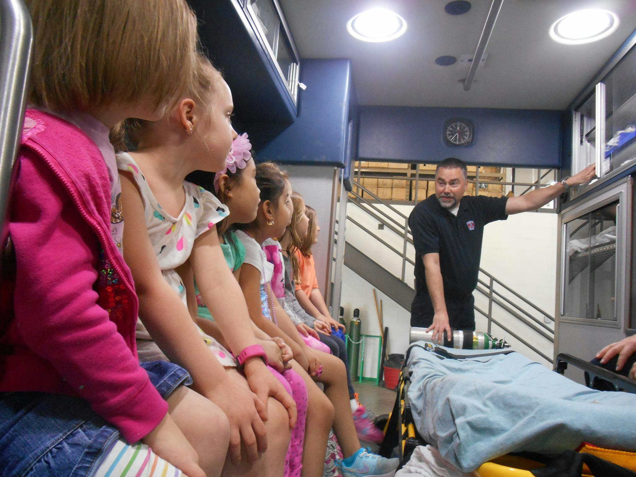 Children sitting in an ambulance with a person standing near a stretcher