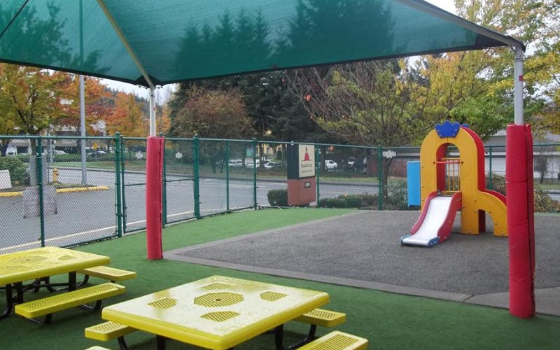 Playground with yellow picnic tables, a green shade, and a small colorful slide
