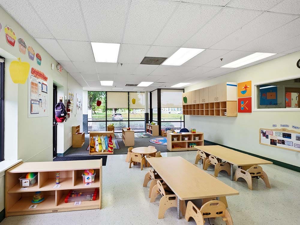 Empty classroom with small tables and chairs, shelves, and large windows