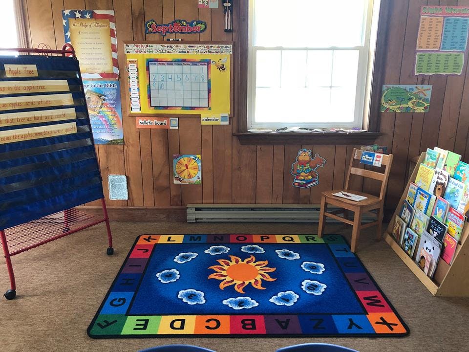 Classroom with a sun and clouds rug, easel, and book display
