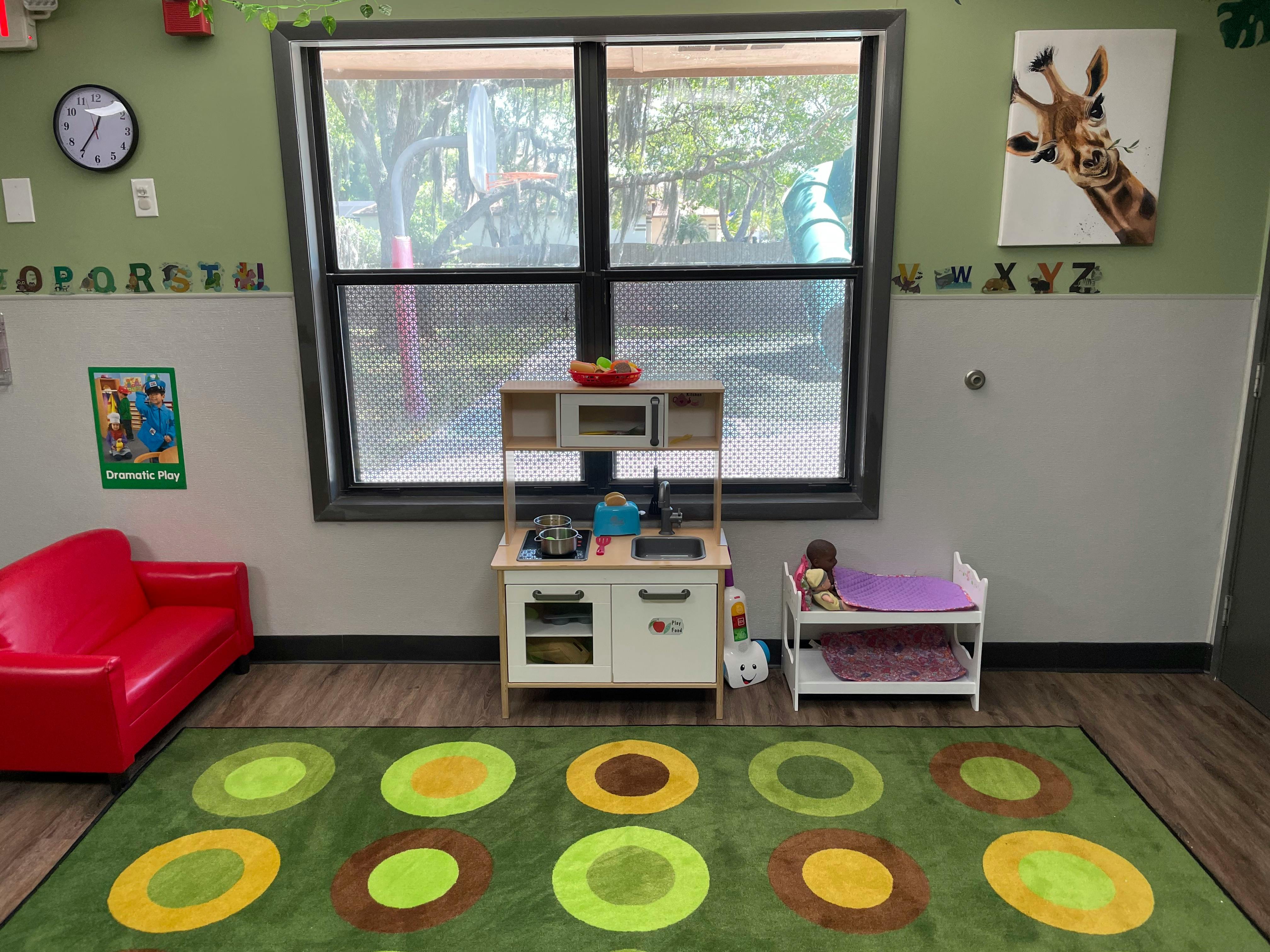 Doll bed and play kitchen in a room with a large window and patterned rug