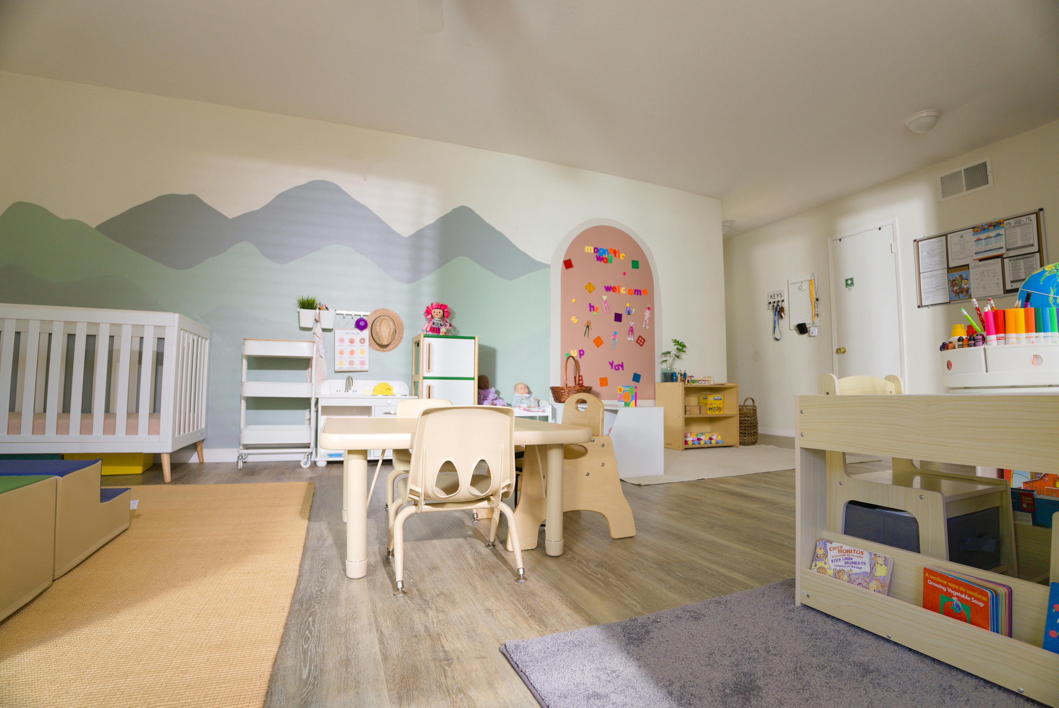 Classroom with a crib, small tables and chairs, a mountain mural, and a magnetic wall