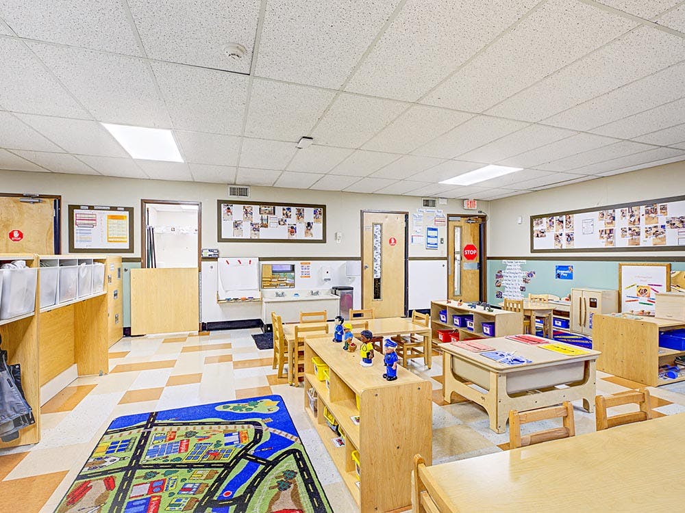 A brightly lit classroom with small wooden tables and chairs
