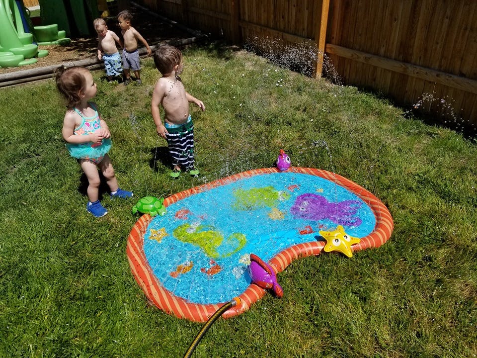 Children playing in a sprinkler pool on grass