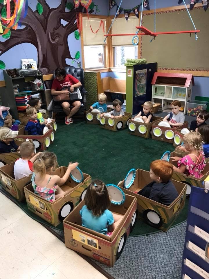 Adult reading to children sitting in cardboard box cars in a classroom