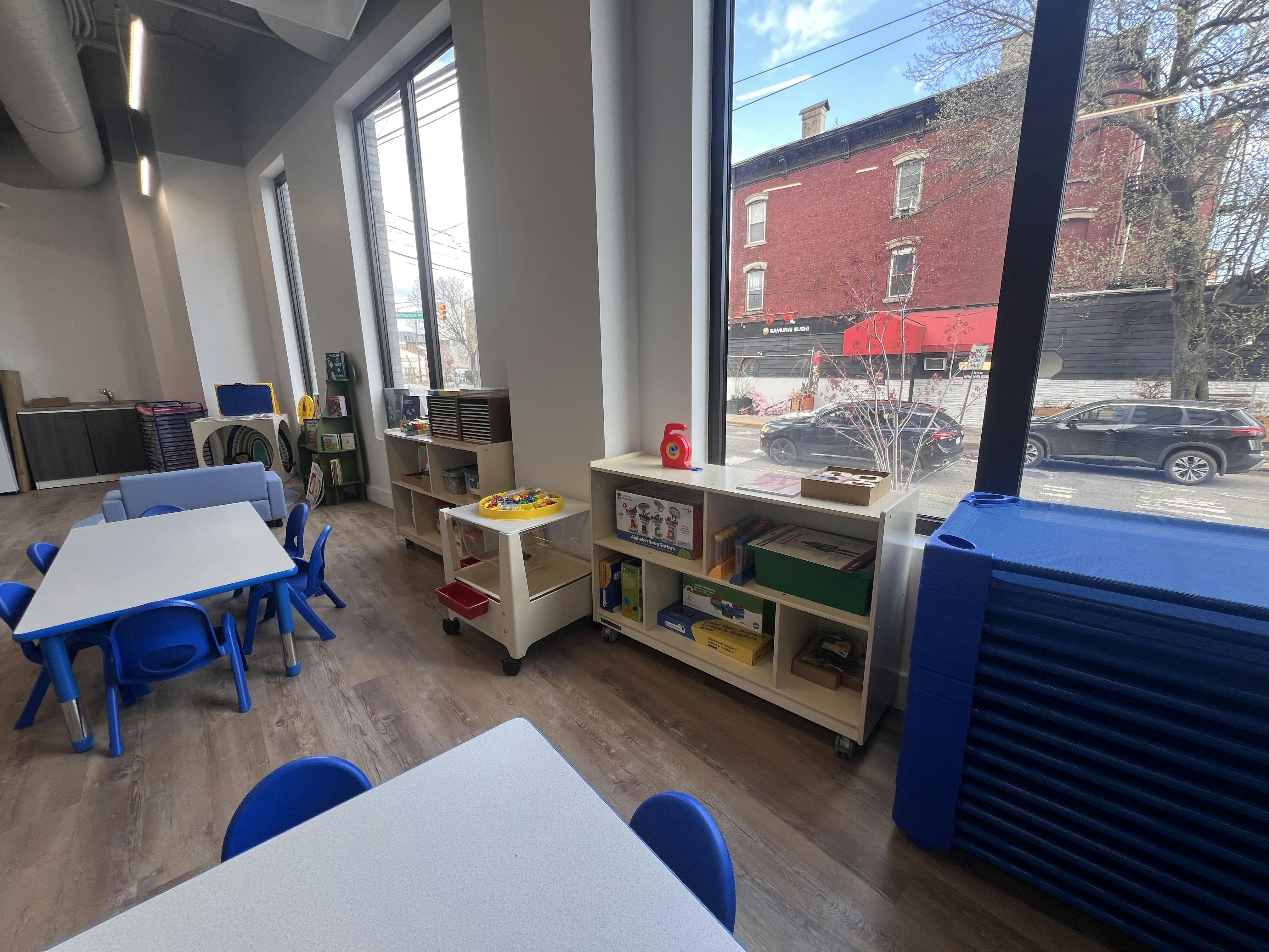 Classroom with child-sized tables and chairs, shelves, and large windows