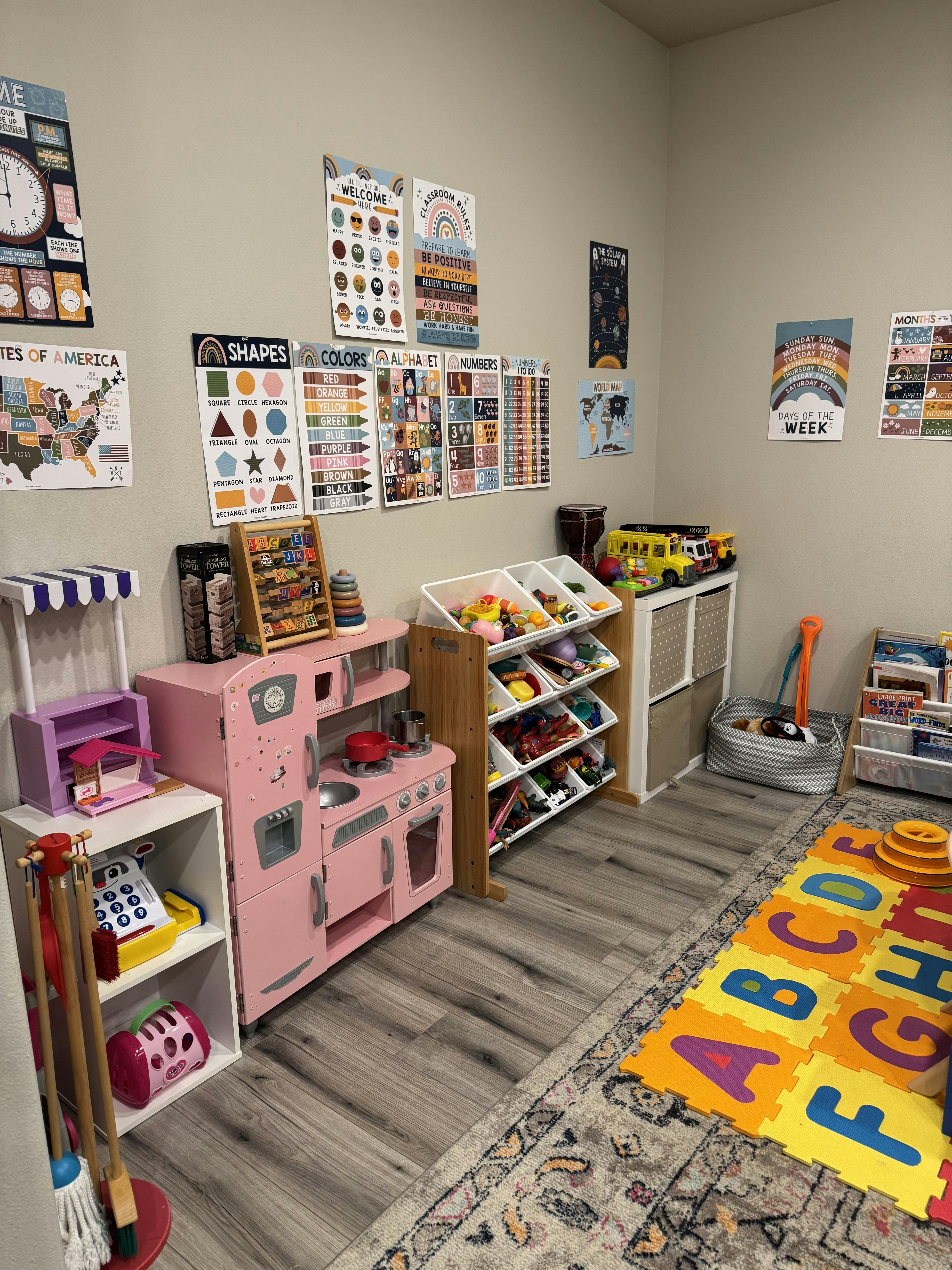Playroom with a pink toy kitchen, toy shelves, and educational posters on the wall