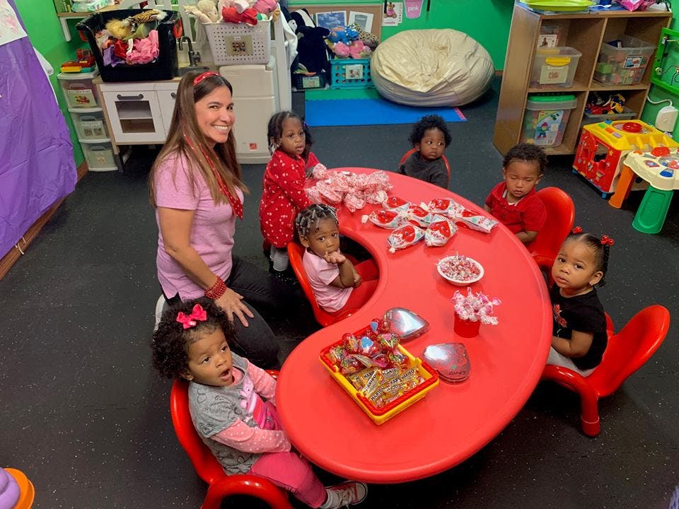 Adult and multiple children sitting around a red table in a classroom