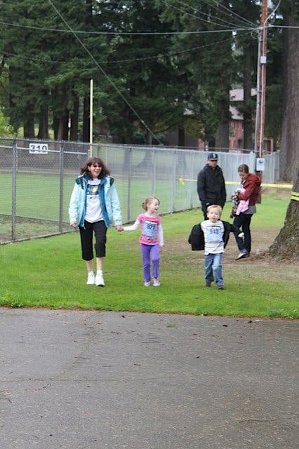 Person walking with two children on grass, other people in background