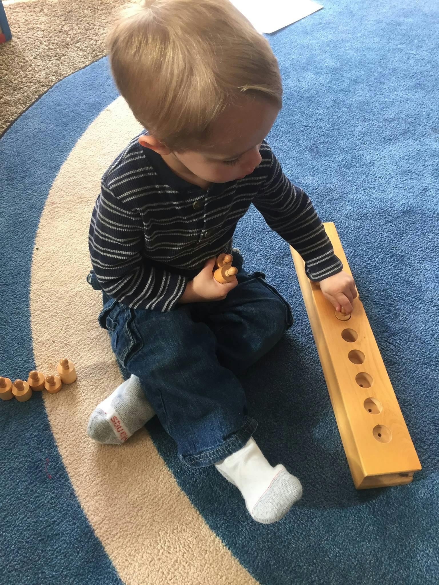Child playing with a wooden peg board on a blue rug