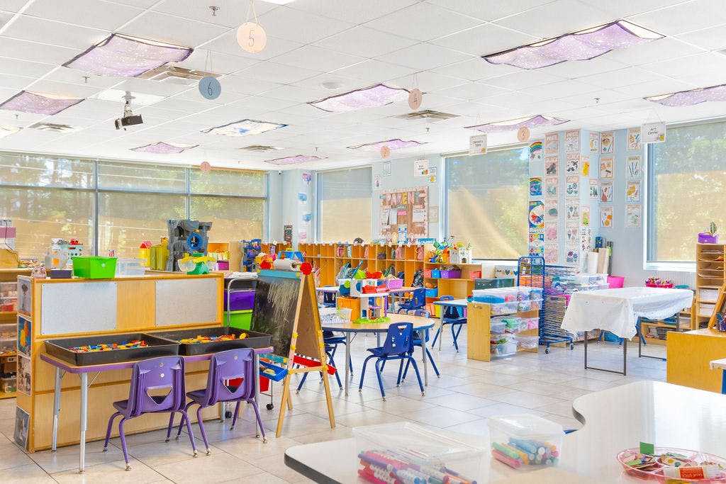 Empty classroom with small tables and chairs, art supplies, and shelves