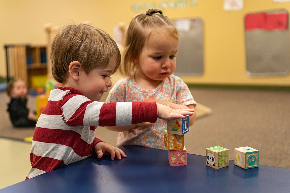 Two children playing with blocks on a table in a classroom