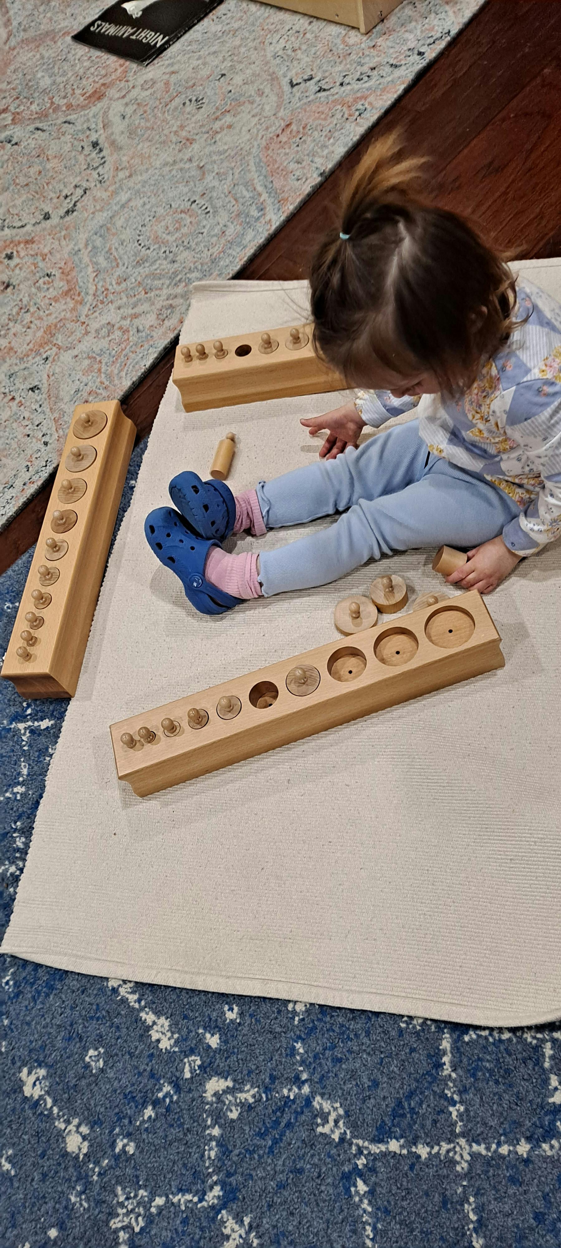 Child playing with wooden cylinder blocks on a mat