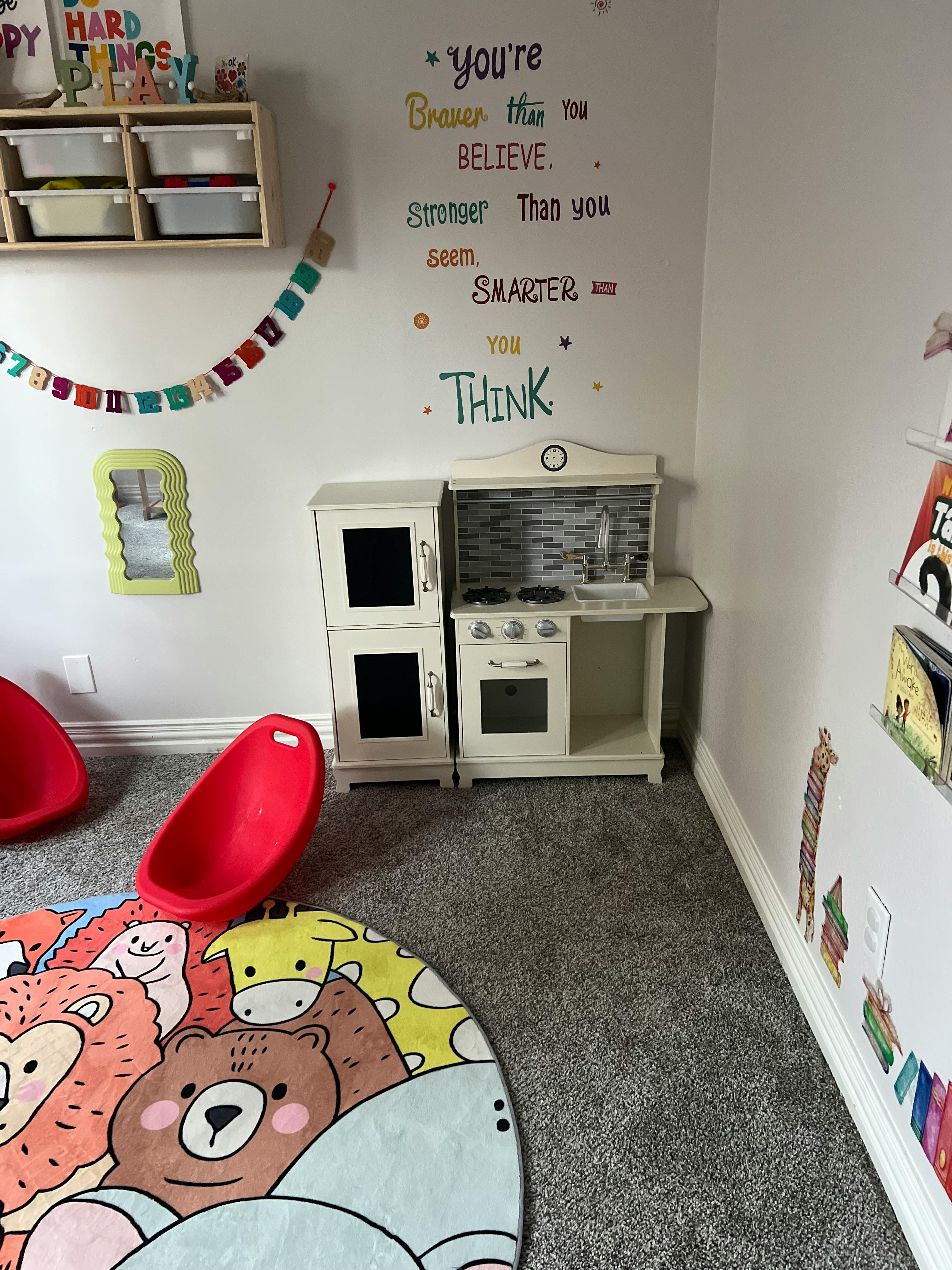 Playroom with toy kitchen, red chairs, and animal rug