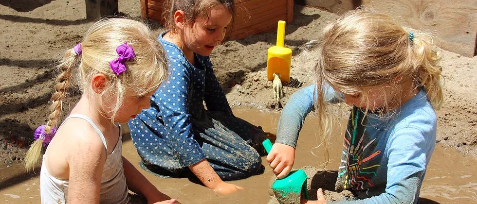 Three children playing in mud with sand toys