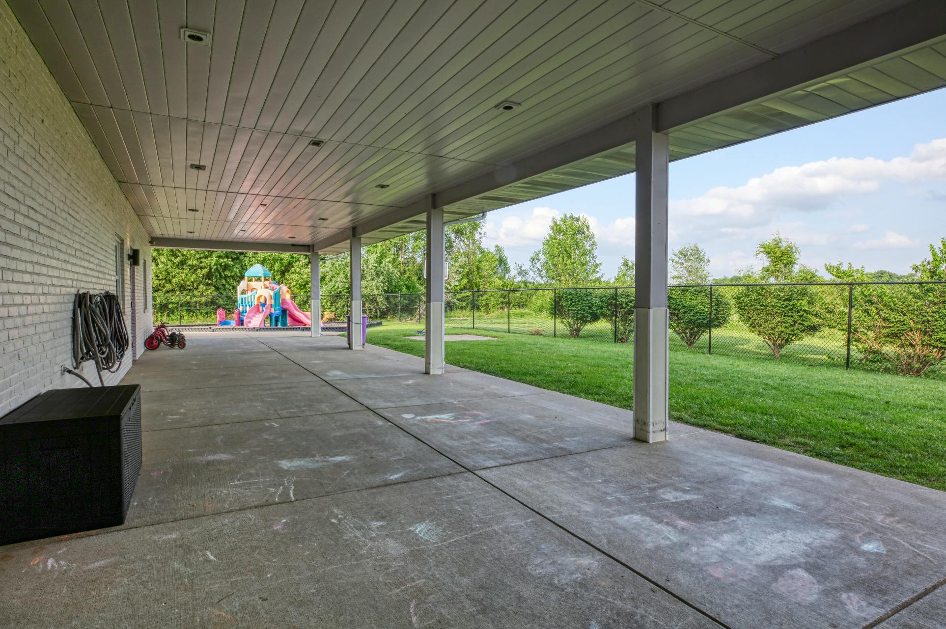 Covered concrete patio with a children's playset visible in the grassy yard