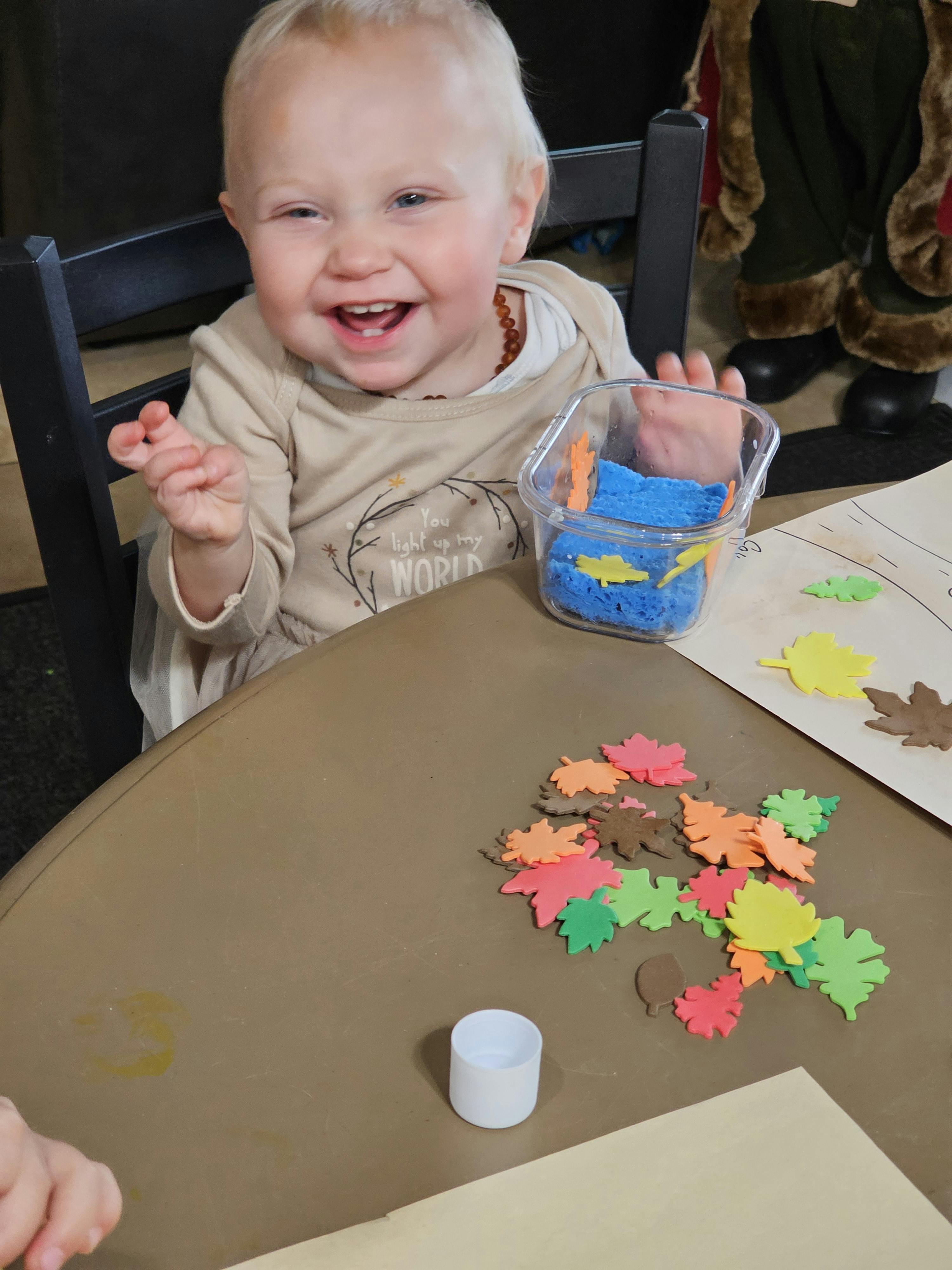 Child at a table with craft supplies, including colorful leaf cutouts