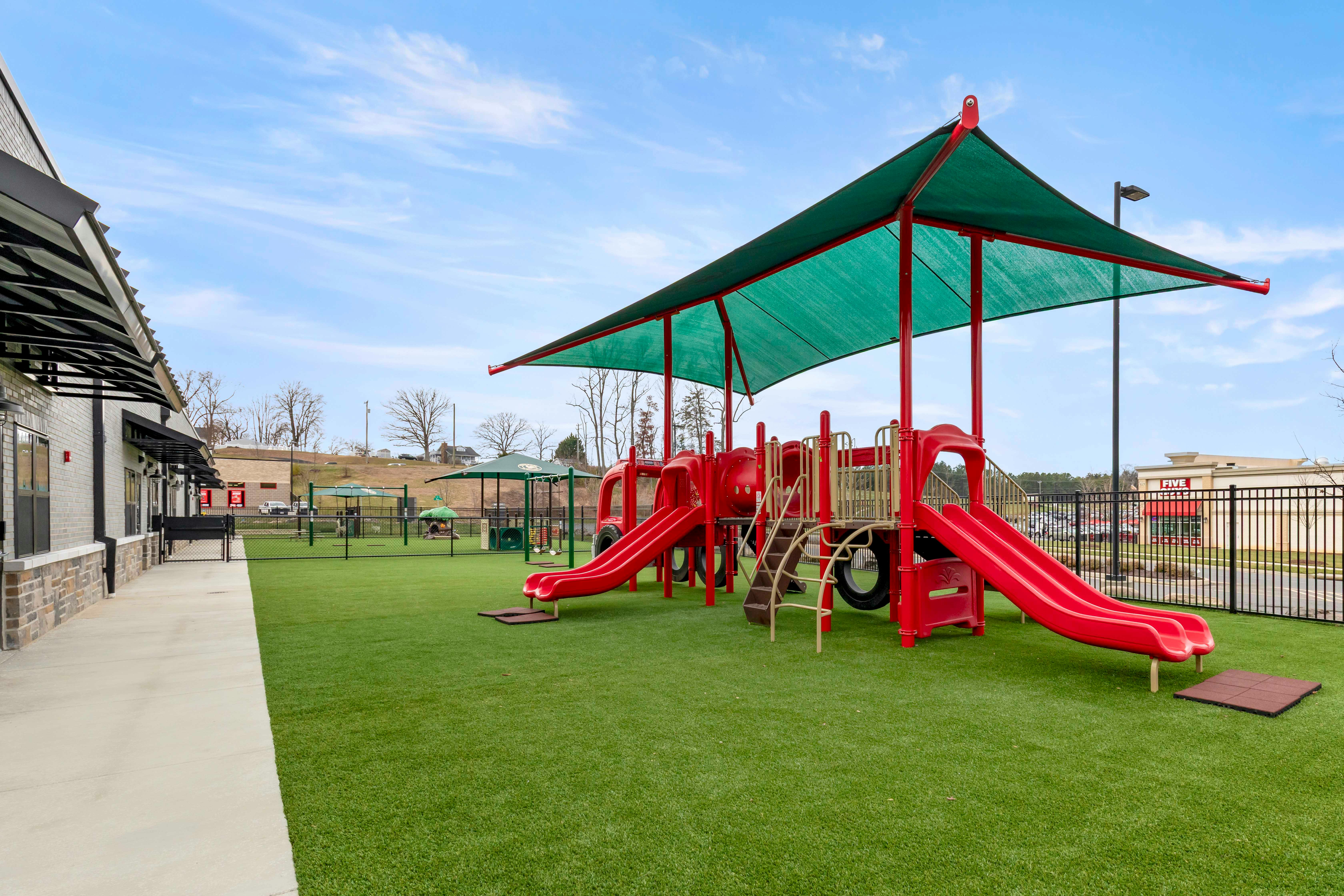 Red playground with slides and climbing structures on green artificial turf