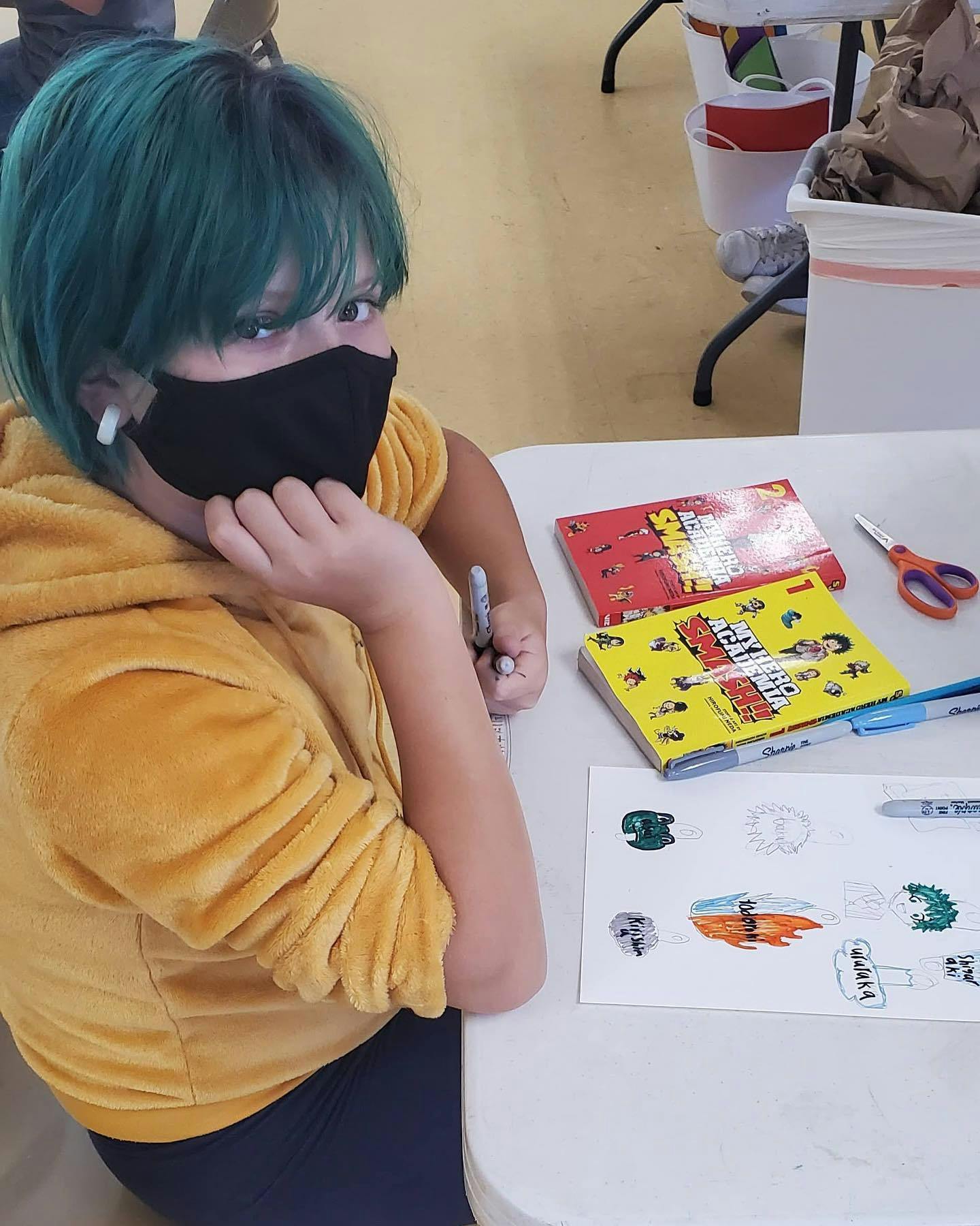 Child with green hair and mask drawing at a table