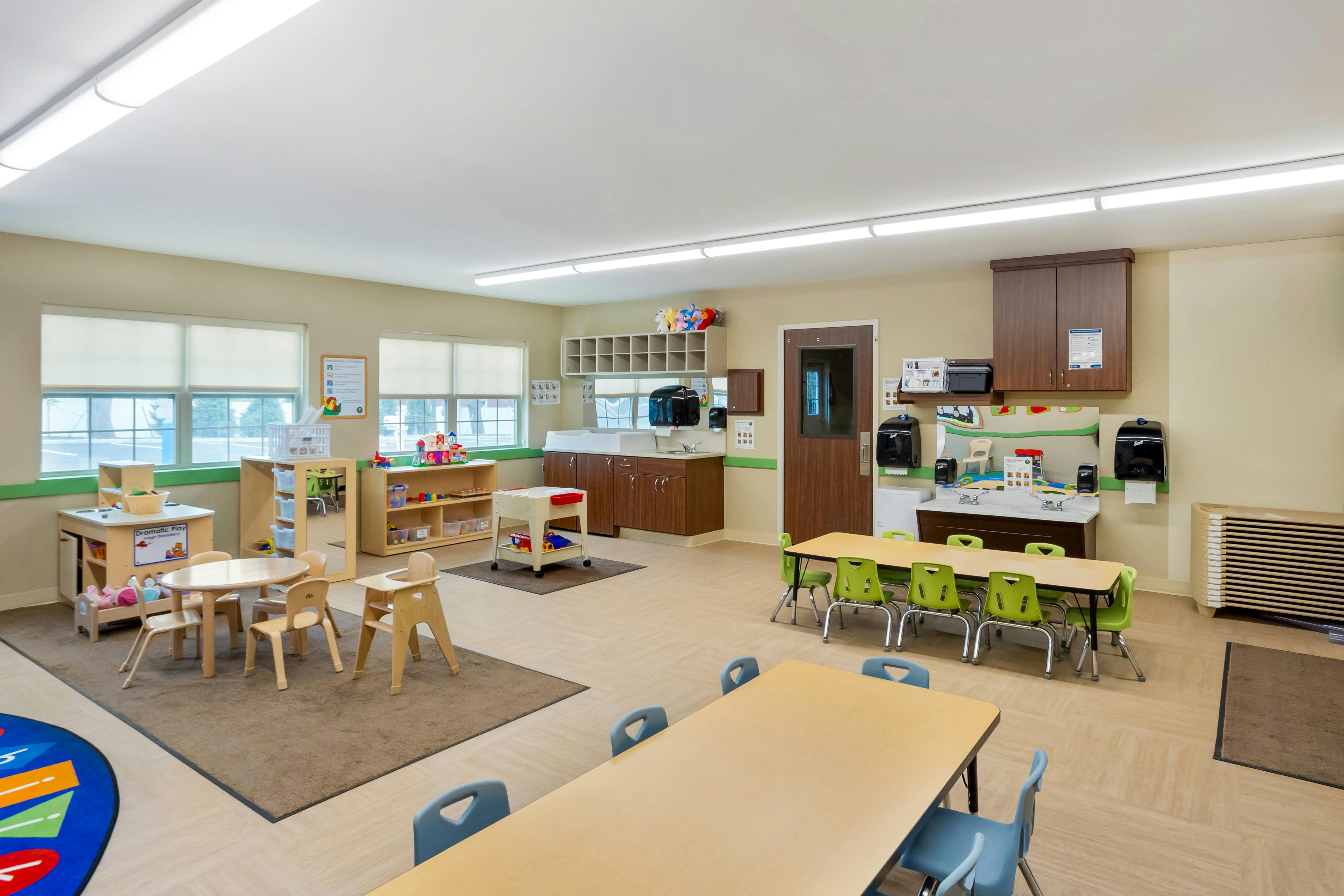 Empty classroom with small tables and chairs, play kitchen, and sinks