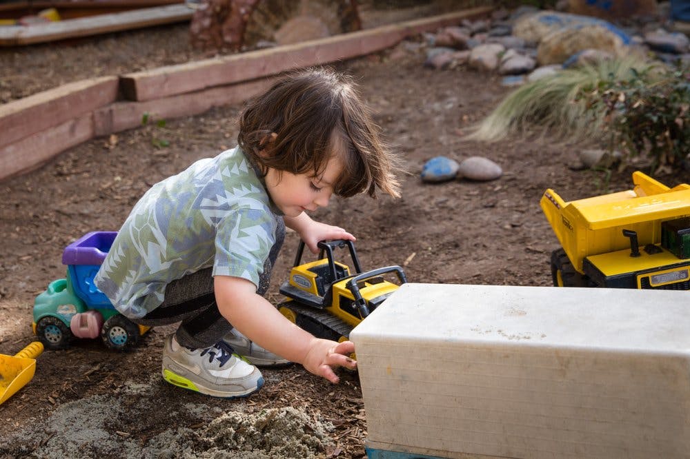 Child playing with toy construction vehicles in dirt
