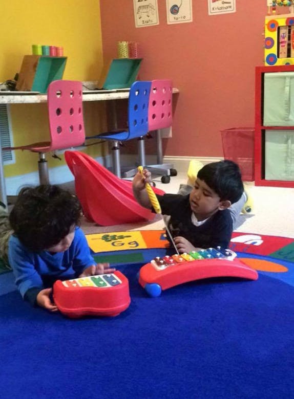 Two children playing with toy xylophones on a blue rug