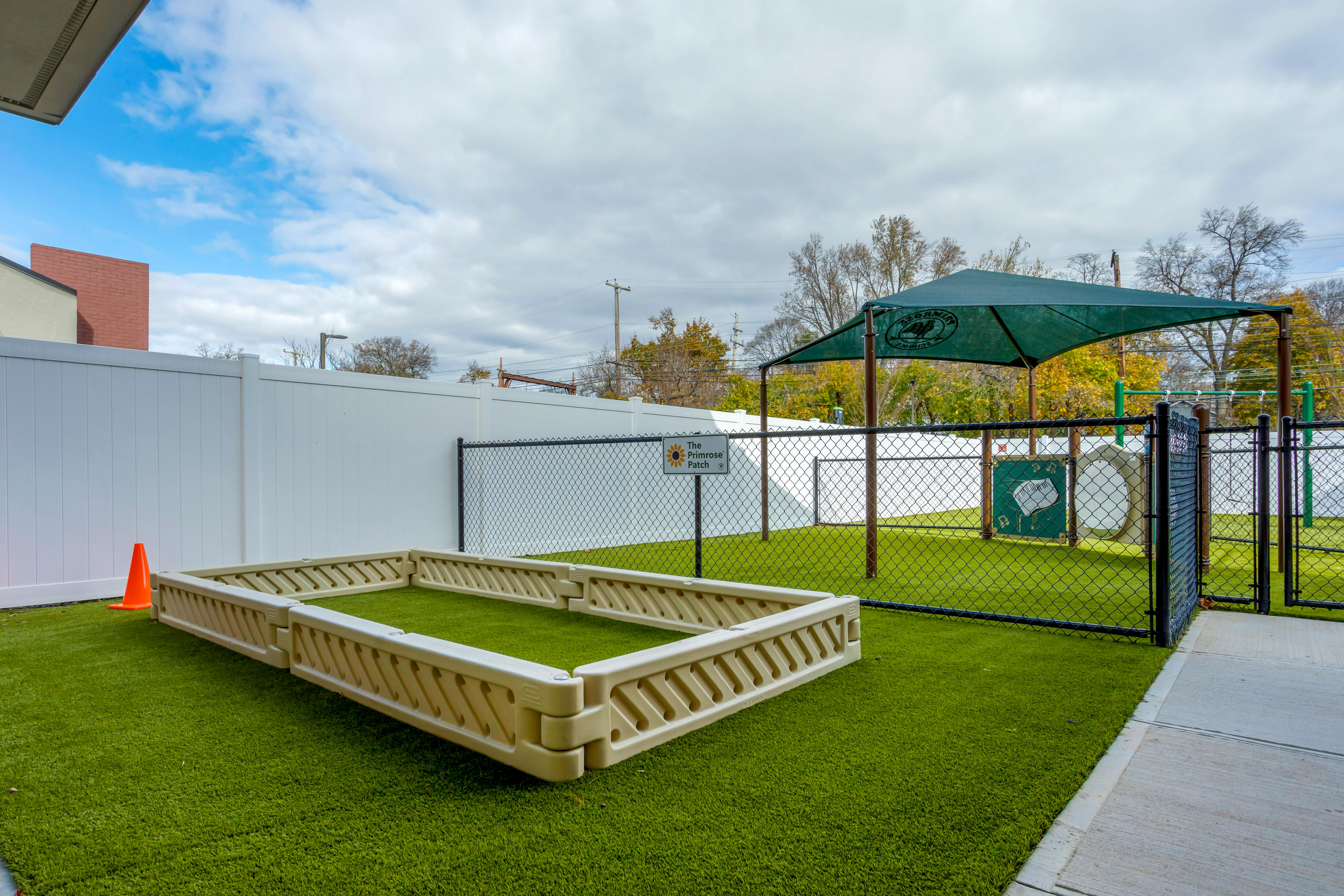 Outdoor play area with green turf, sandpit, and play structure with shade cover