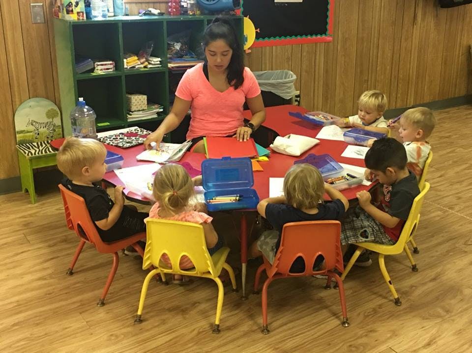 Person at a table with multiple children in a classroom