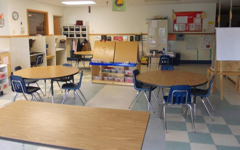 Classroom with round and rectangular tables and chairs, art supplies, and cubbies
