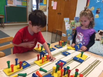 Two children playing with colorful pegboard toys at a table