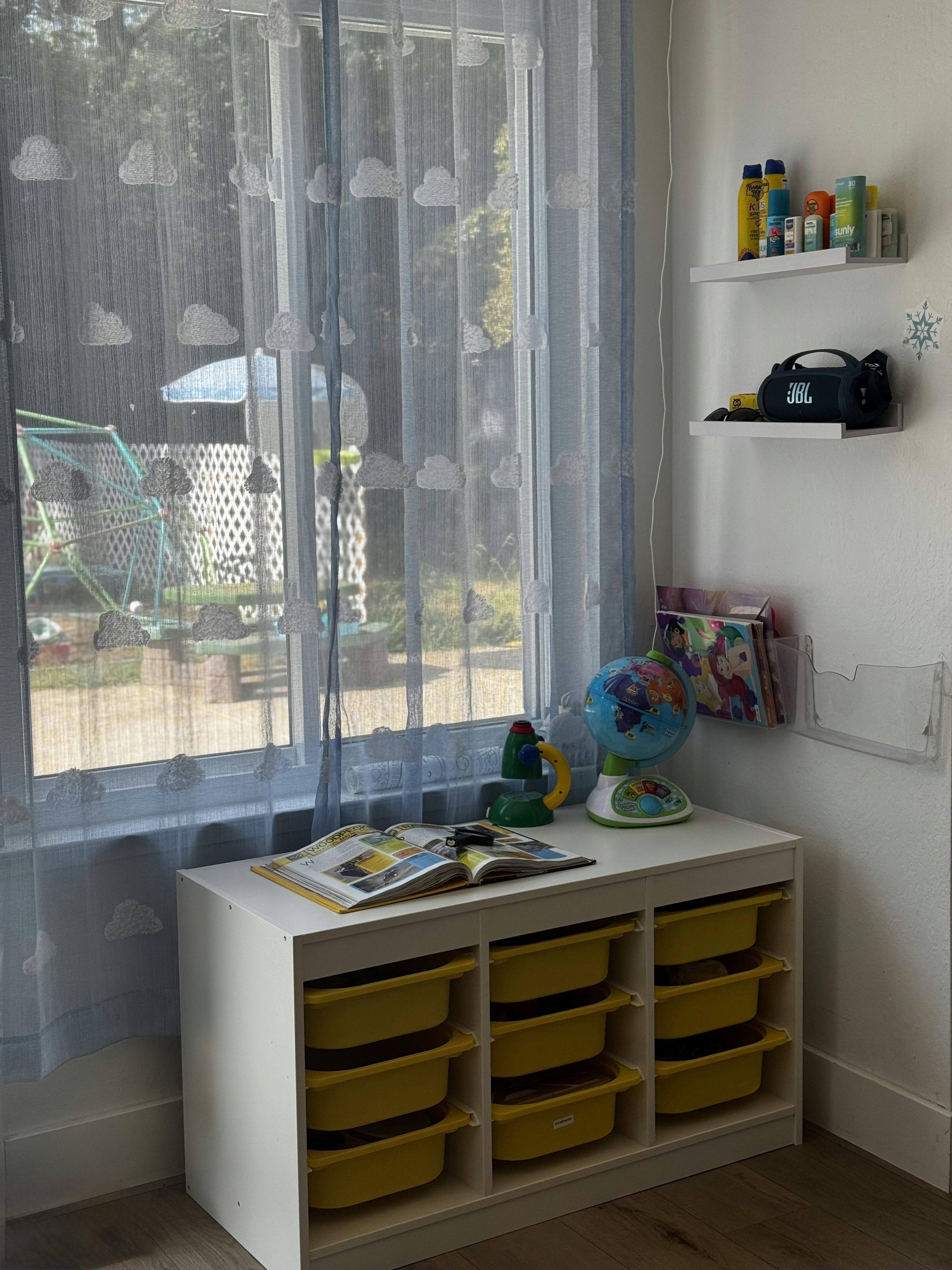 White storage unit with yellow bins under a window with cloud-patterned curtains