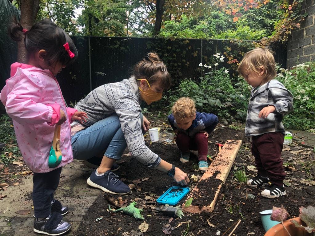 Person and two children playing in dirt with toys