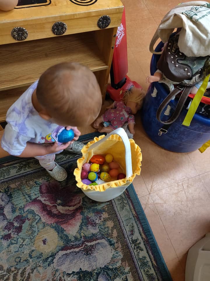 Child holding a blue egg over a basket of colorful eggs