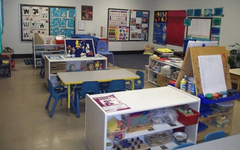 A classroom with tables, chairs, shelves of supplies, and artwork on the walls