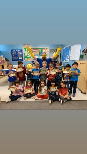 Person in superhero costume with children holding certificates in a classroom