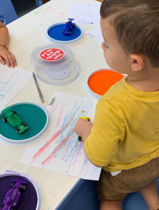 Child using a toy car to make colorful tracks on paper