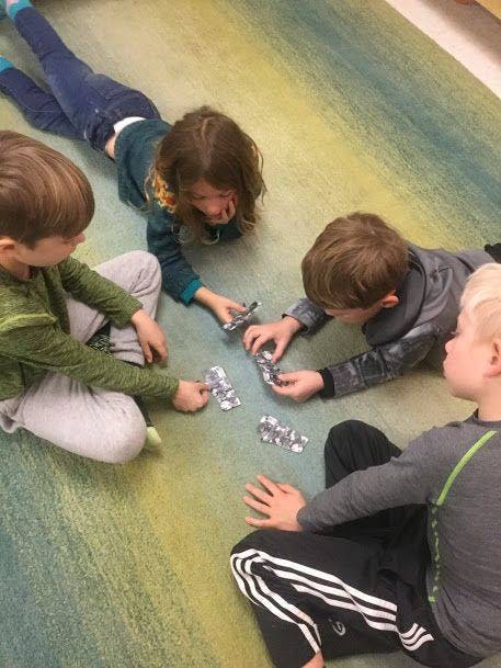 Four children playing with small objects on a carpeted floor