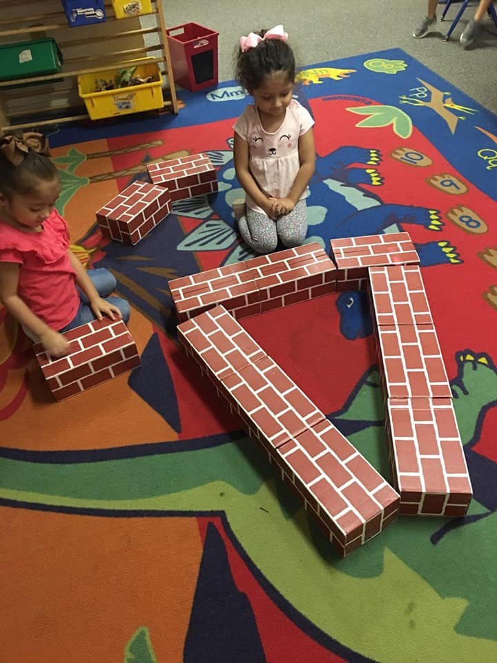 Two children playing with brick-patterned blocks on a colorful rug