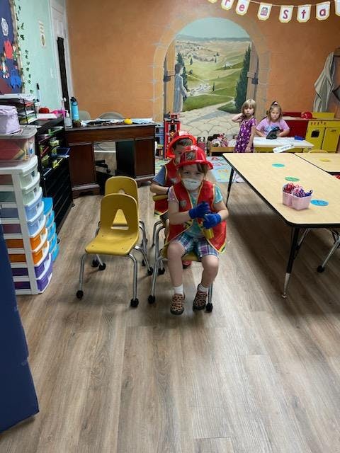 Child in a firefighter costume and mask sitting on a chair in a classroom