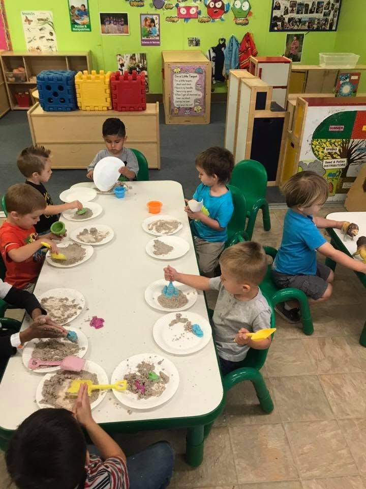 Children playing with sand and small toys at a table in a classroom