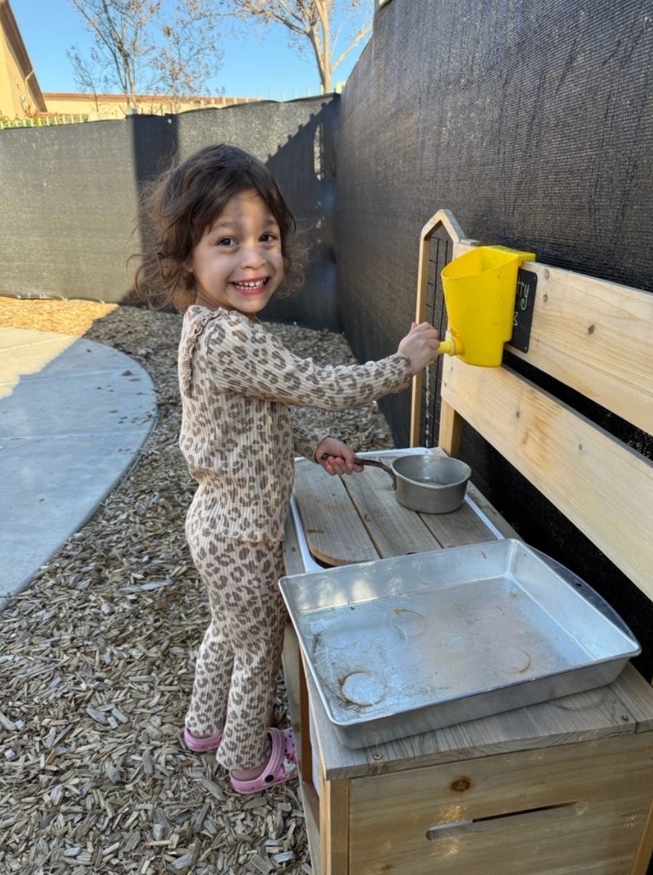 Child pouring water from a yellow pitcher into a pot