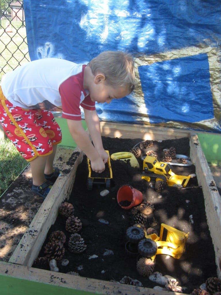 Child playing with toy trucks in a dirt pit