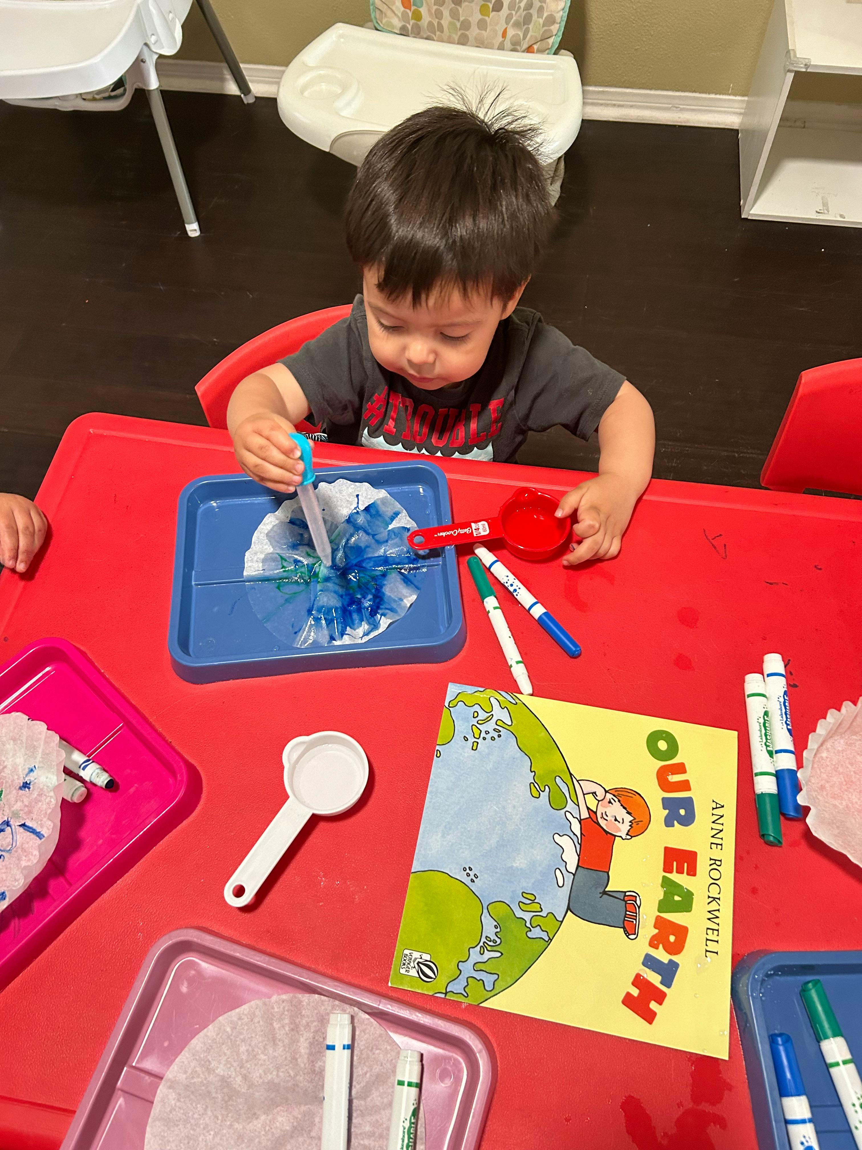 Child at a red table doing an art activity with markers and paper