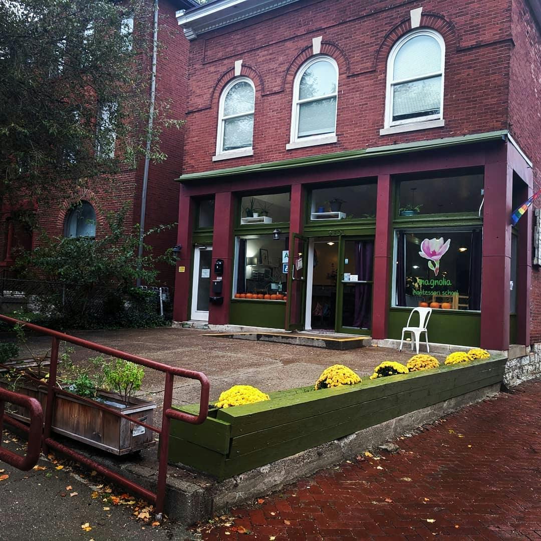 Red brick building with storefront windows and a green planter with yellow flowers
