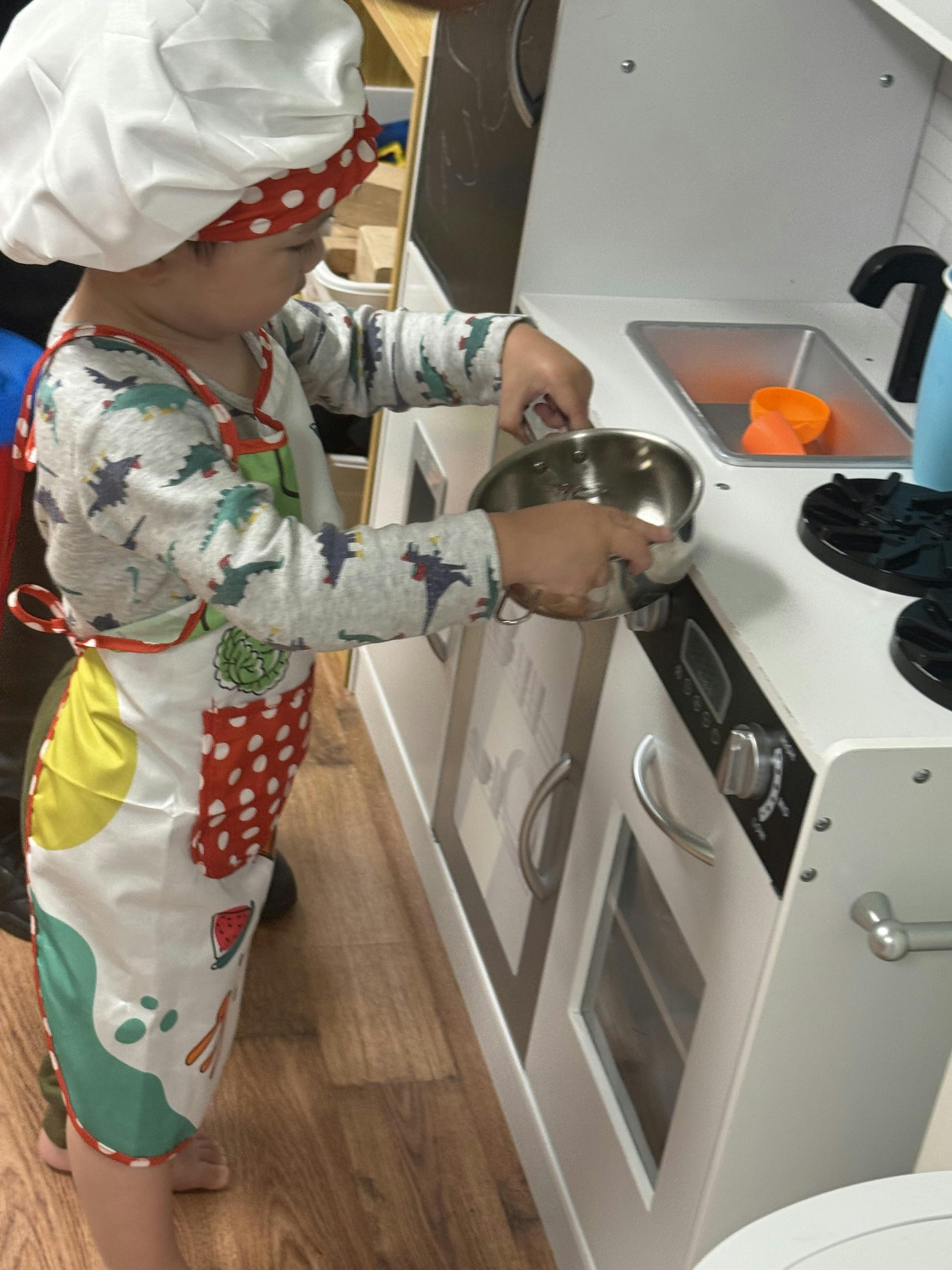 Child wearing a chef hat and apron playing with a toy kitchen