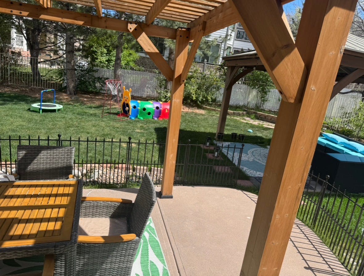 Backyard patio with wooden pergola and dining furniture overlooking a lawn